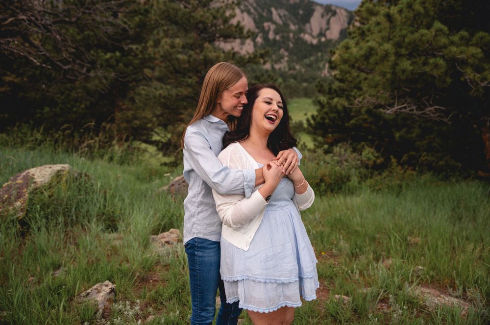 Two people share a joyful moment together while standing in a grassy meadow with mountains in the background.