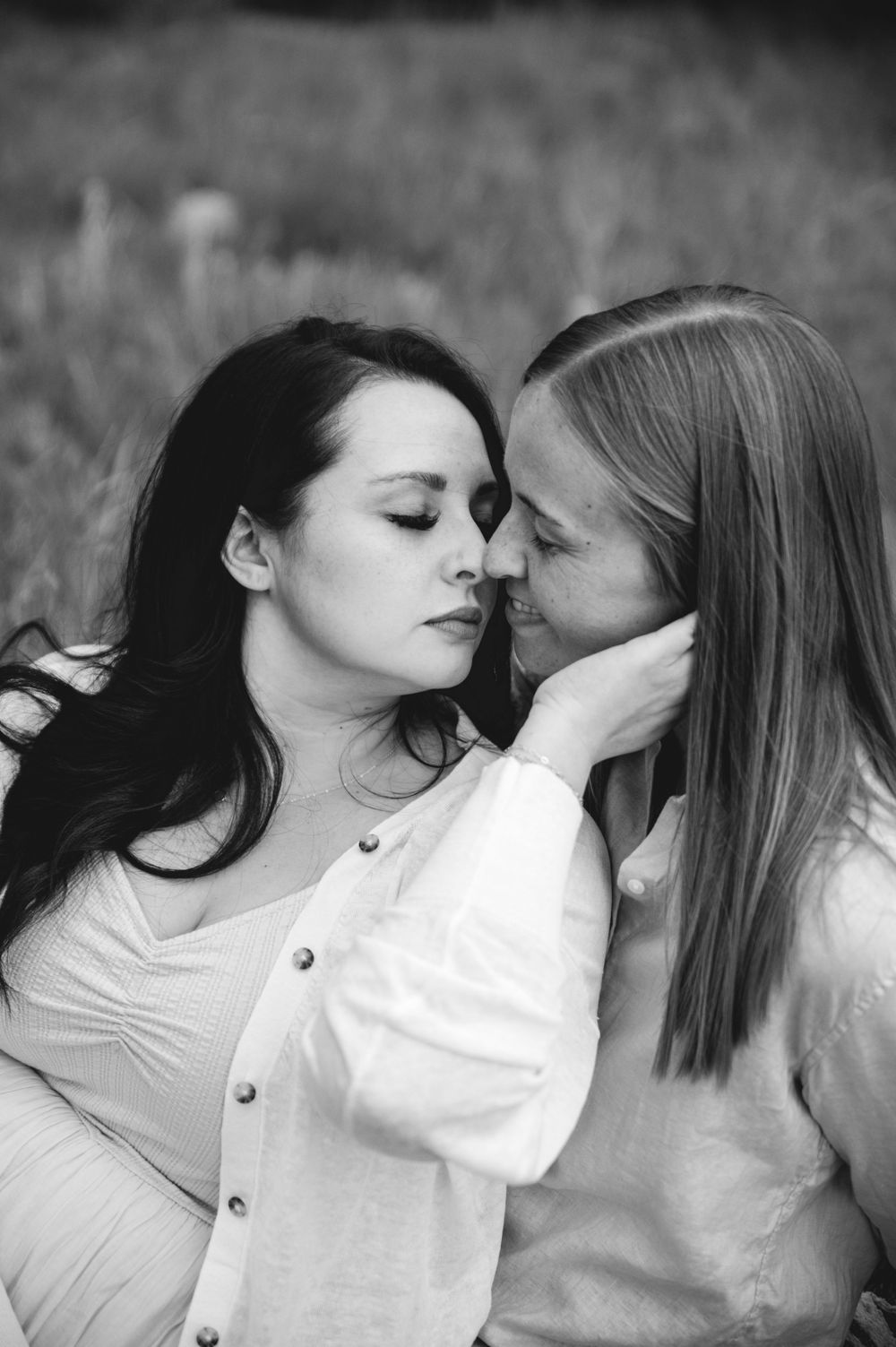 Black and white photo of an intimate romantic moment between two people in white clothing sitting together outdoors.