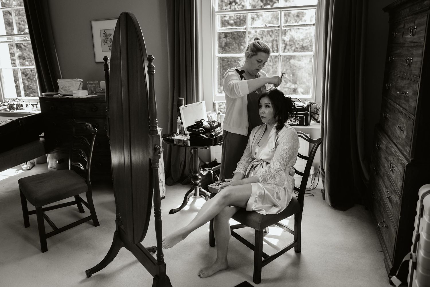 A black and white photograph showing two people in an intimate parlor setting with a large full-length mirror.