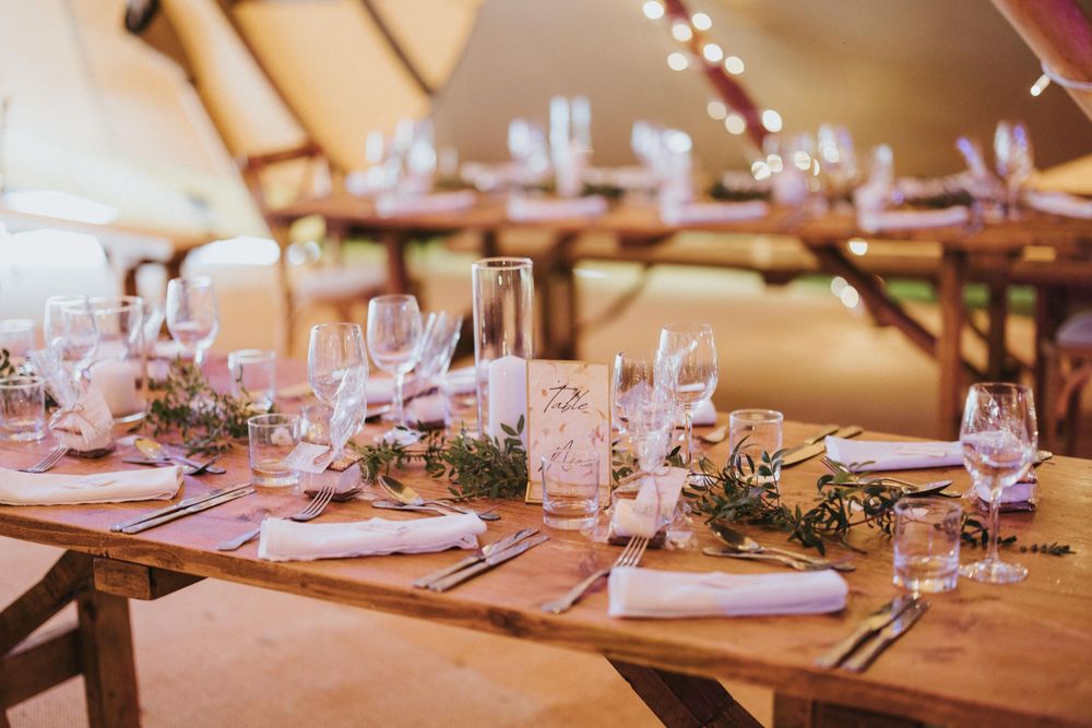 Elegant reception tables set with white linens, wine glasses, and natural greenery centrepieces in a warm-lit venue at Hirst Priory.