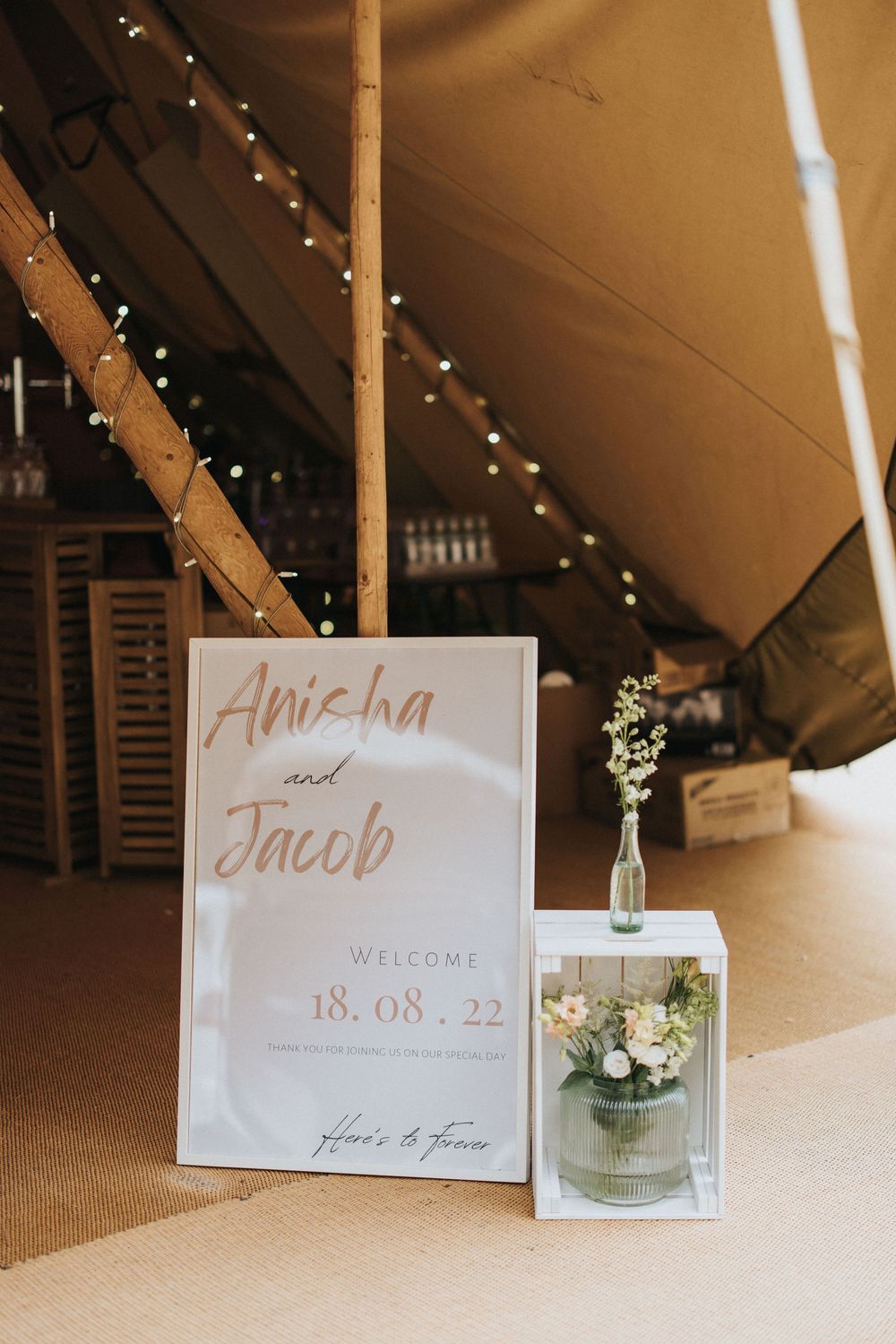 Wedding welcome sign and name cards displayed with small flower vases at a reception under warm lighting at Hirst Priory.