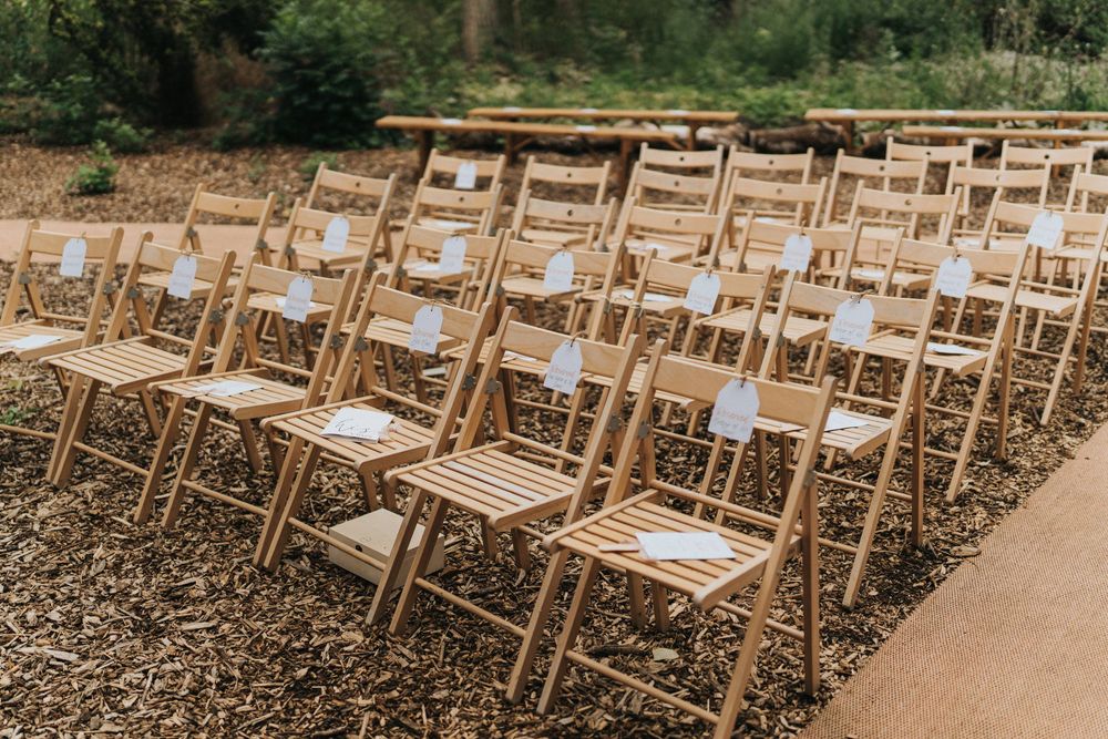 Rows of wooden folding chairs set up for an outdoor wedding event in a natural garden setting at Hirst Priory.