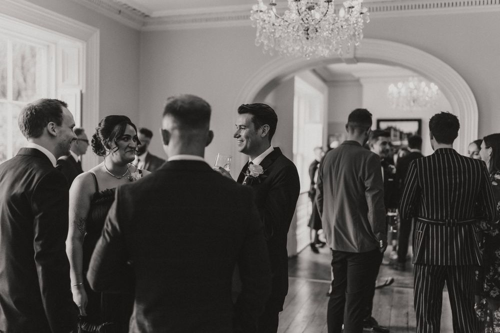 Wedding guests gathered in an elegant room with chandelier and arched doorway at Hirst Priory - taken by Grimsby photographers.