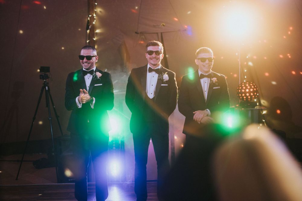Three performers in tuxedos on stage with dramatic lighting and bokeh effects during wedding venue at Hirst Priory.