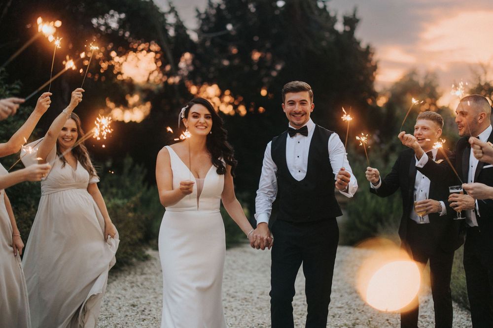 Wedding party celebrates with sparklers during golden hour sunset in outdoor wedding celebration at Hirst Priory.