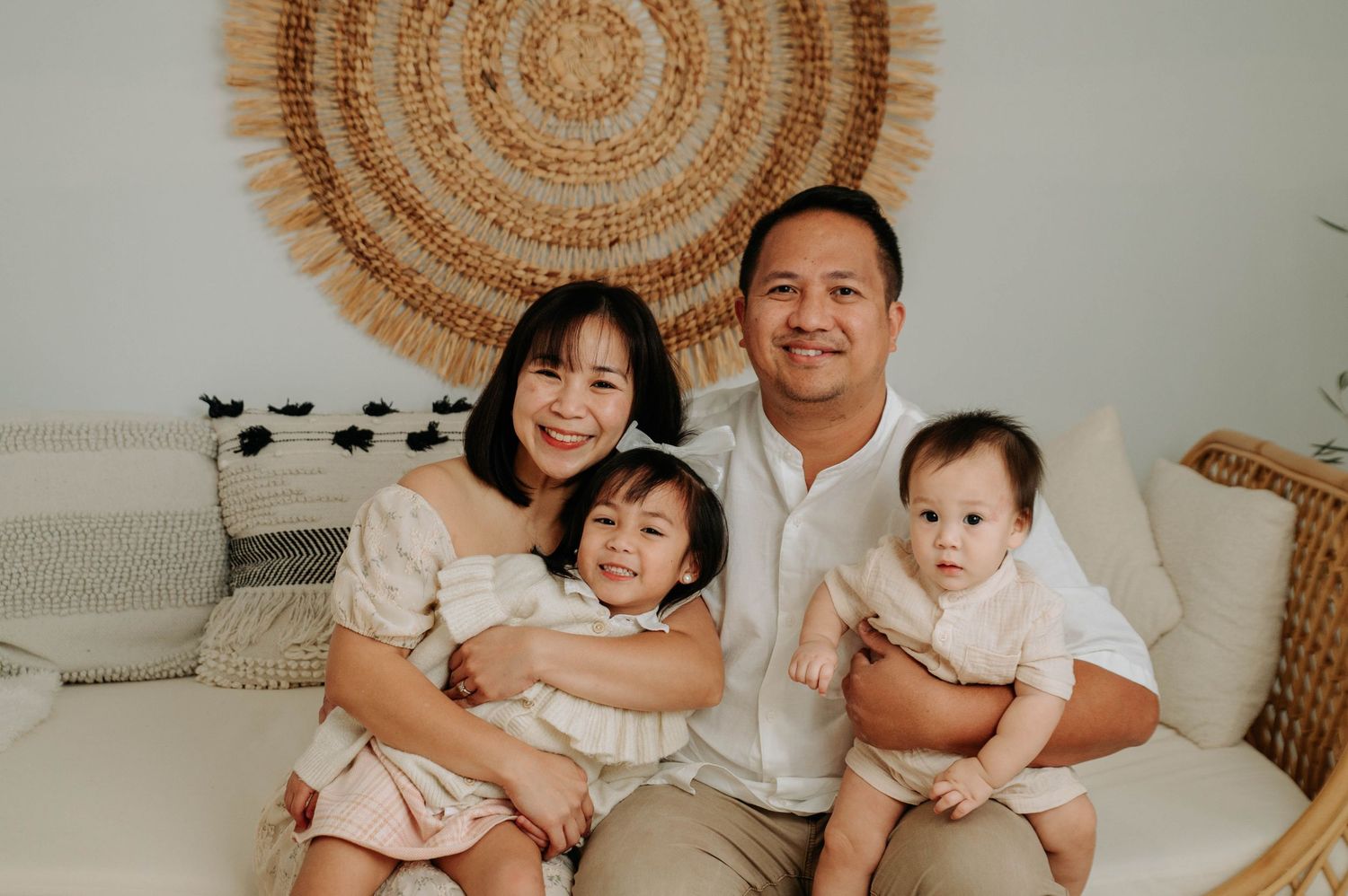 Studio portraits with neutral beige backdrop featuring loving family moments and circular woven boho wall decor.