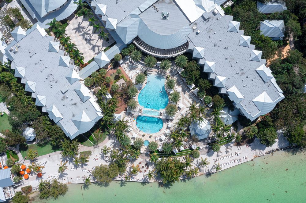 Aerial view of a luxury beachfront resort with tropical landscaping, central swimming pools, and direct access to turquoise waters and sandy