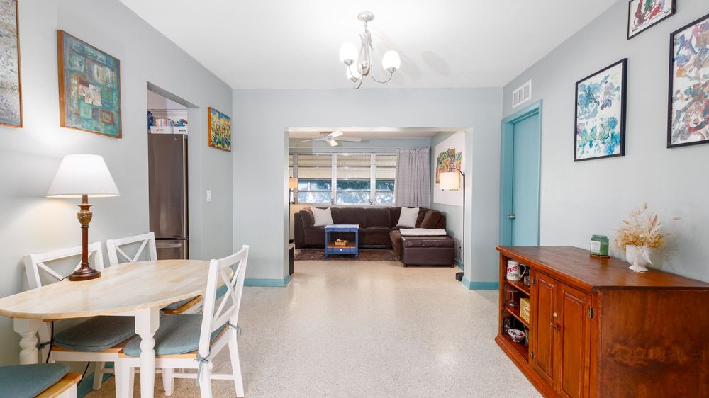 Charming open-layout dining and living room with vintage décor, pastel blue accents, and natural light flowing through large front windows.