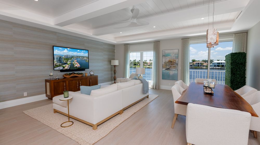 Elegant waterfront living and dining space with coastal-inspired décor, white seating, wood dining table, and panoramic views through glass
