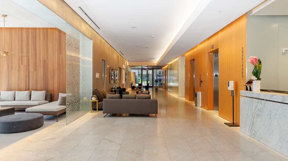 Modern commercial or residential lobby with marble flooring, wood-paneled walls, contemporary seating, and a reception area near elevator