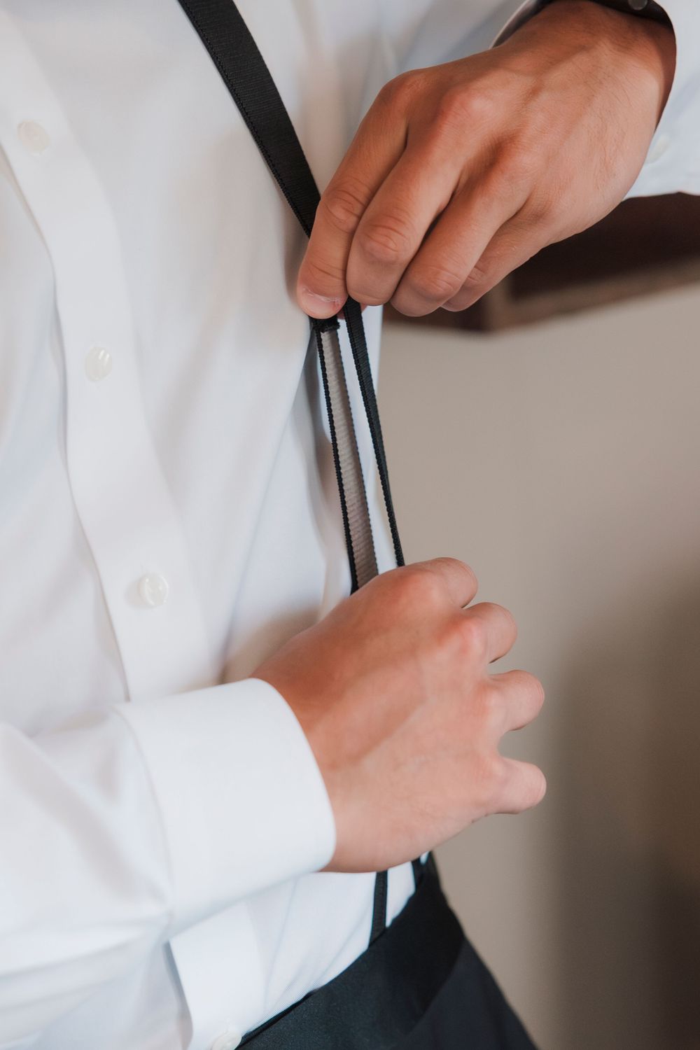 Close-up of hands adjusting a black necktie against a white dress shirt.