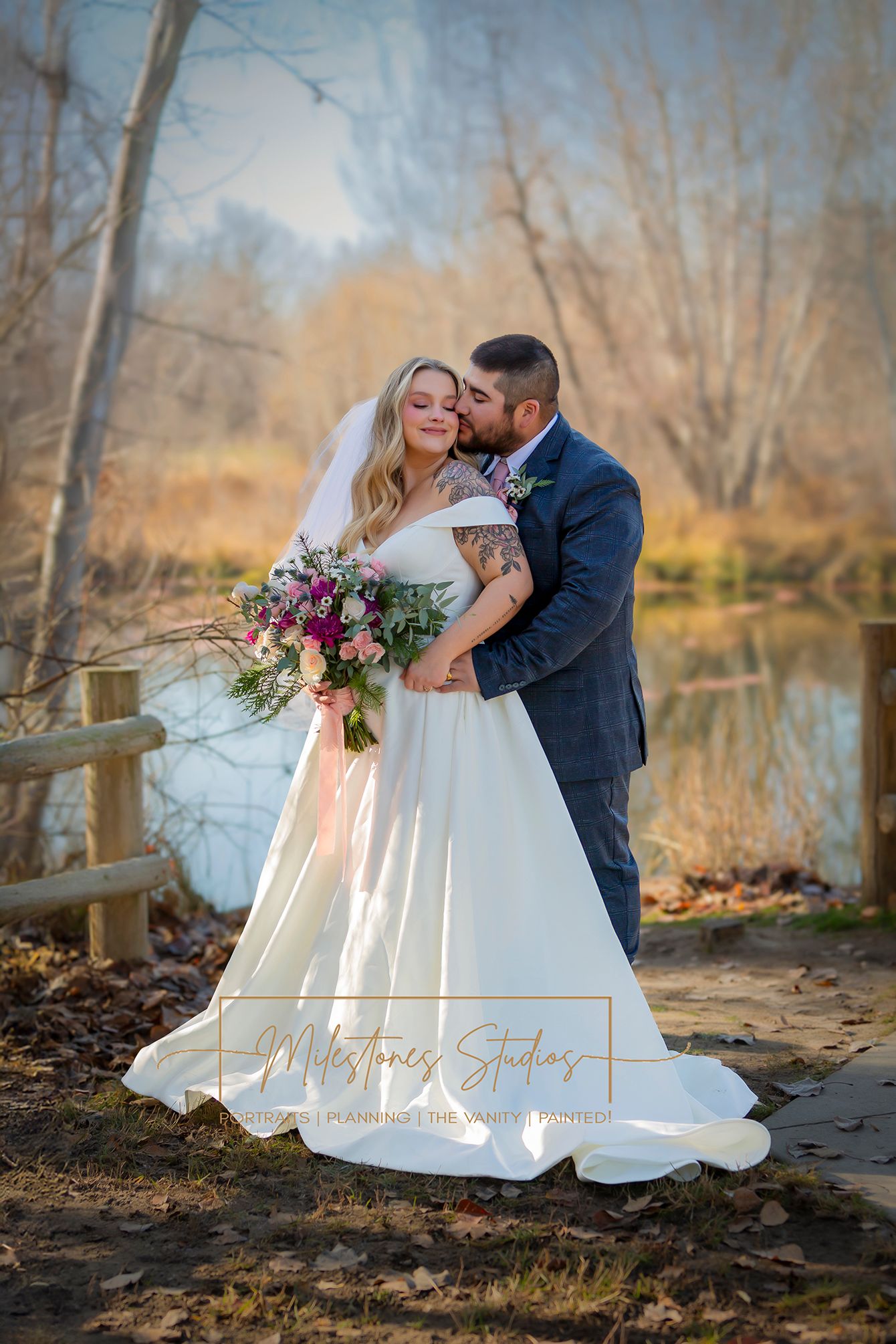 wedding portrait groom kissing bride's cheek in front of pond