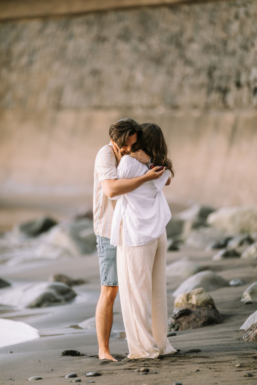 A series of serene beach photographs showing two figures embracing against a rocky coastal backdrop at sunset.