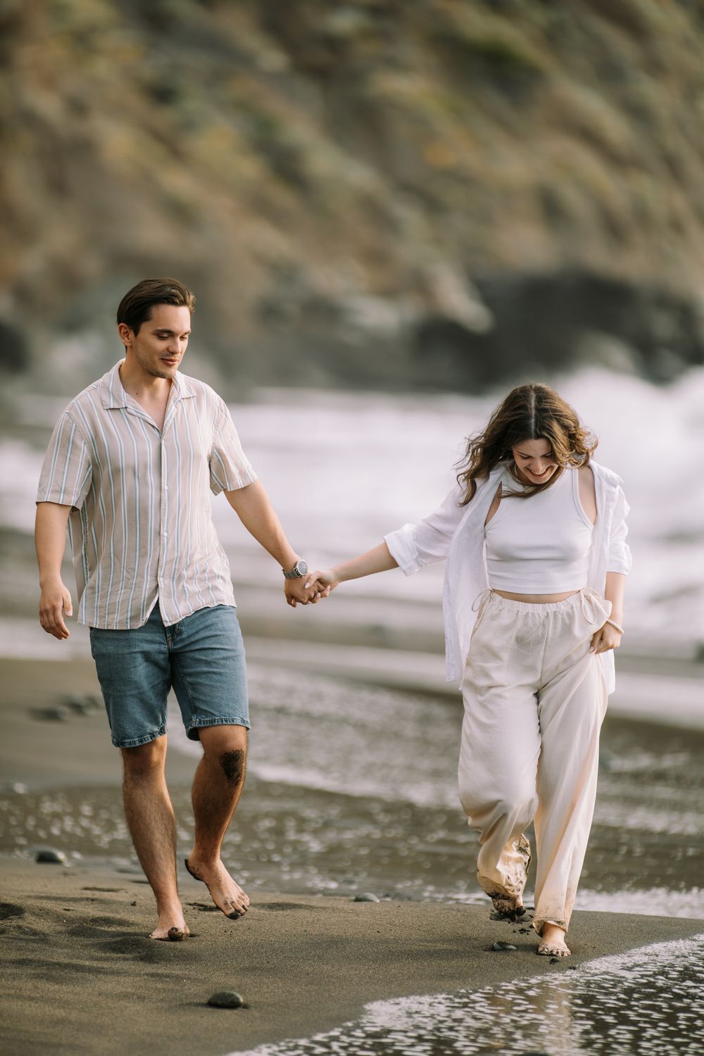 A couple walks barefoot along the shoreline together as waves gently lap at their feet on a serene beach.