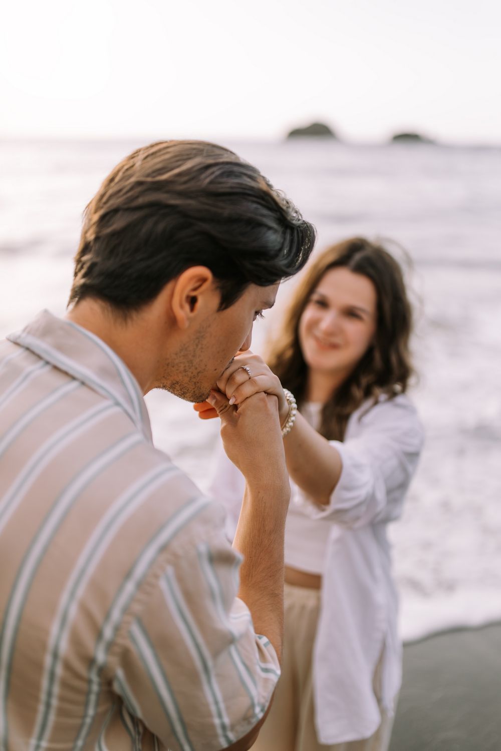 A couple walking together on a beach and playfully interacting during a romantic sunset photoshoot.