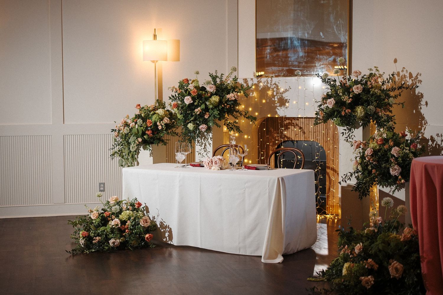 Wedding reception venue decorated with elegant floral arrangements, warm lighting, and white tablecloths in a rustic space.