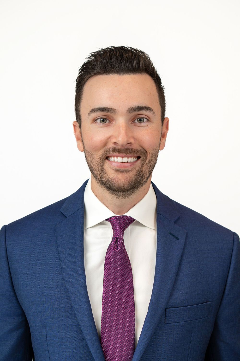 Professional portrait of a male lawyer wearing a navy suit and purple tie on white background.