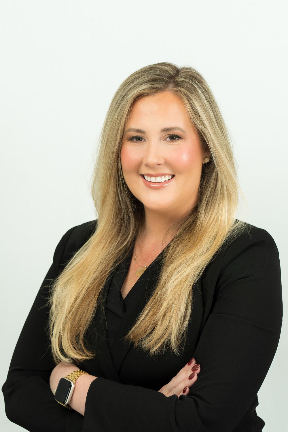 Professional headshot of a blonde woman lawyer in a black blazer smiling with arms crossed against white background.