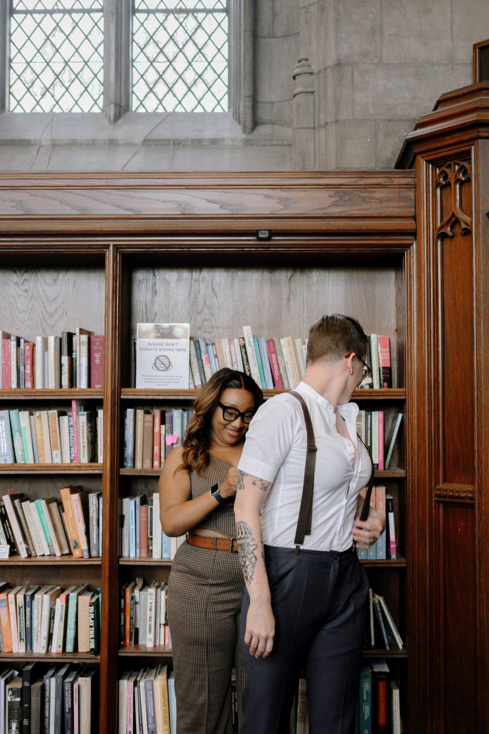 A couple browsing books together in a library with vintage wooden bookshelves and a diamond-paned window.