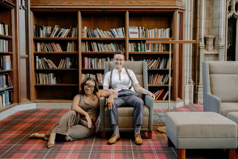 Several people relaxing in comfortable armchairs and couches in a cozy library with floor-to-ceiling bookshelves.