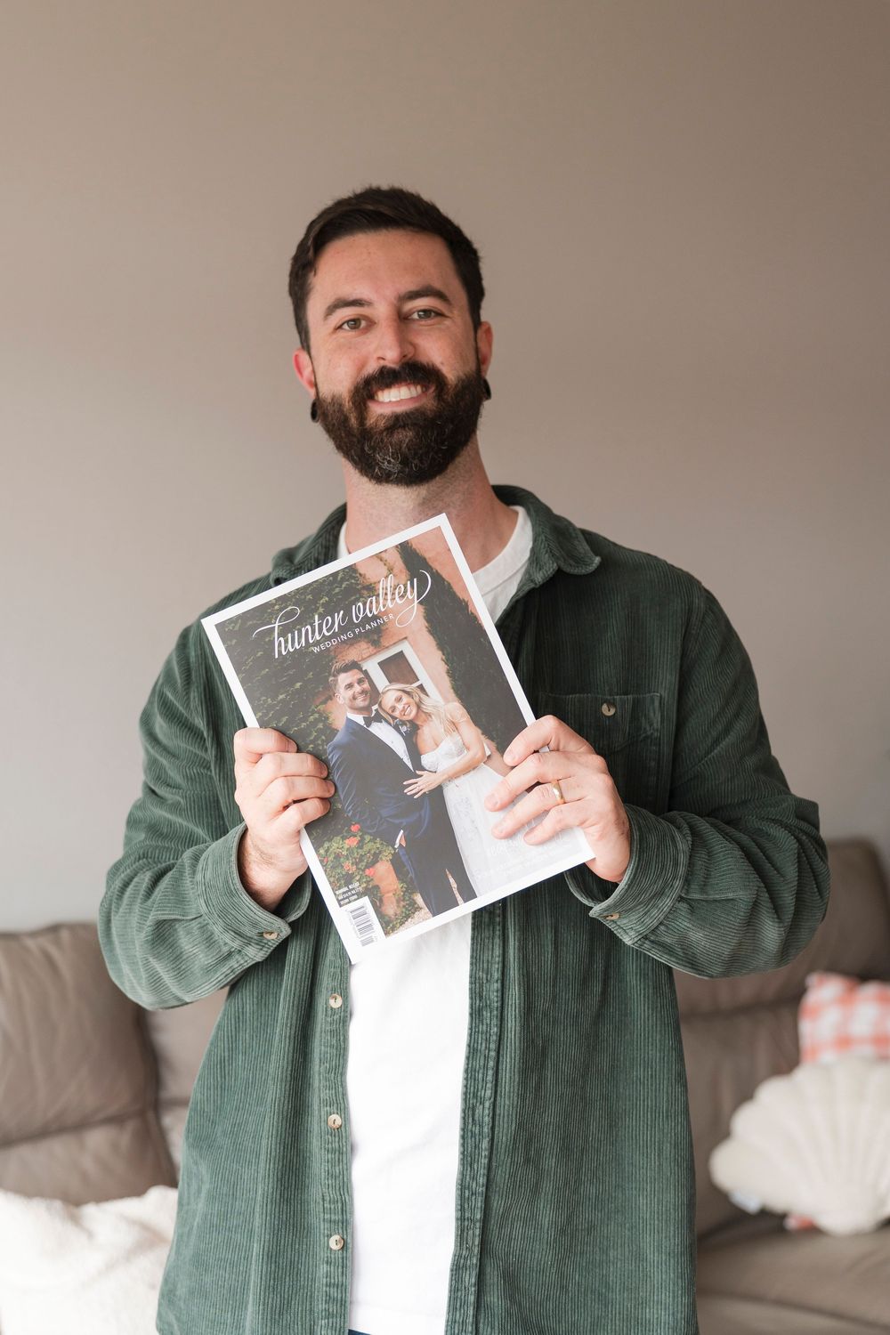 A person wearing a green corduroy shirt holds up a photo album while standing in a living room setting.