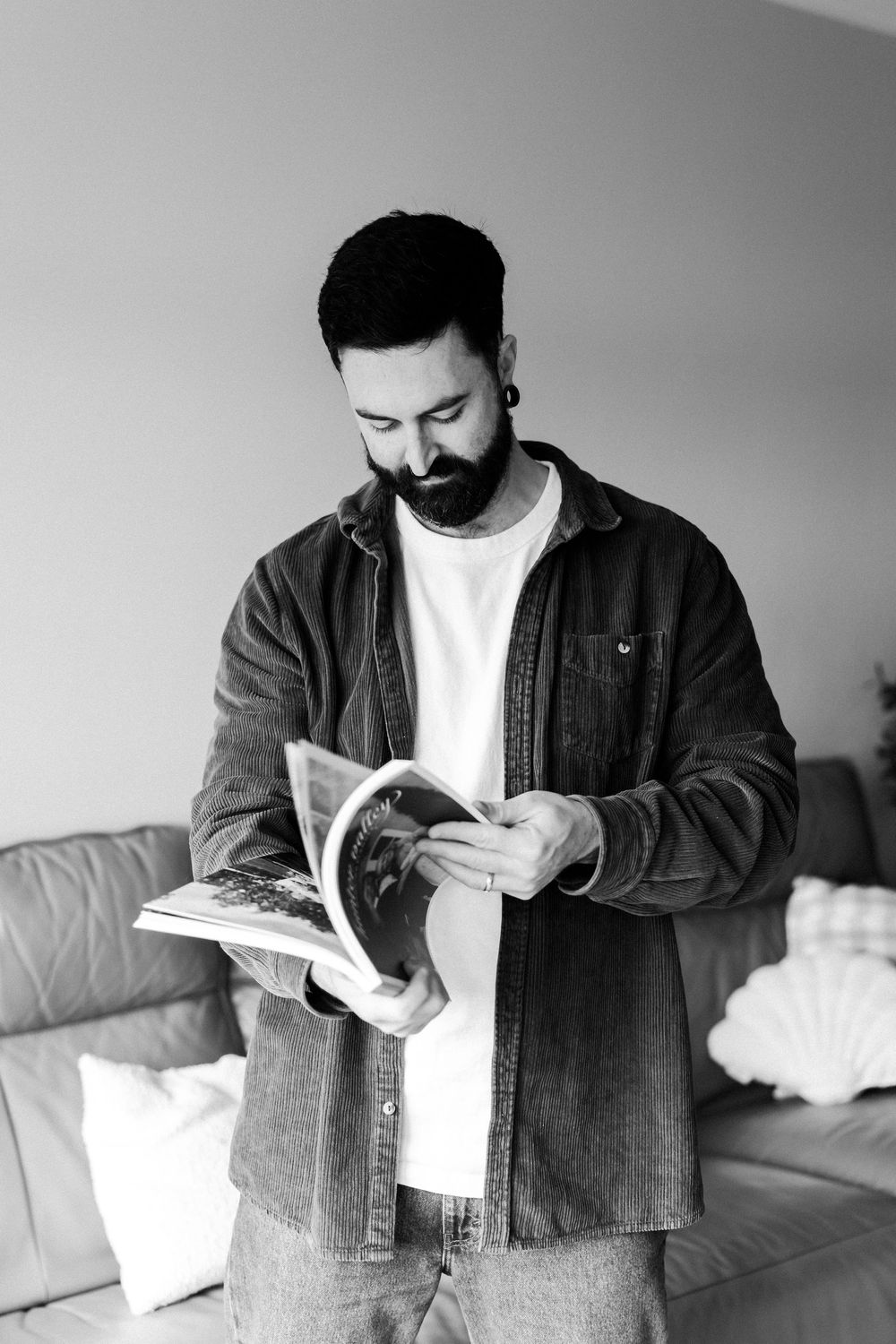 A man in denim jacket looks through pages of a book while standing in a room.