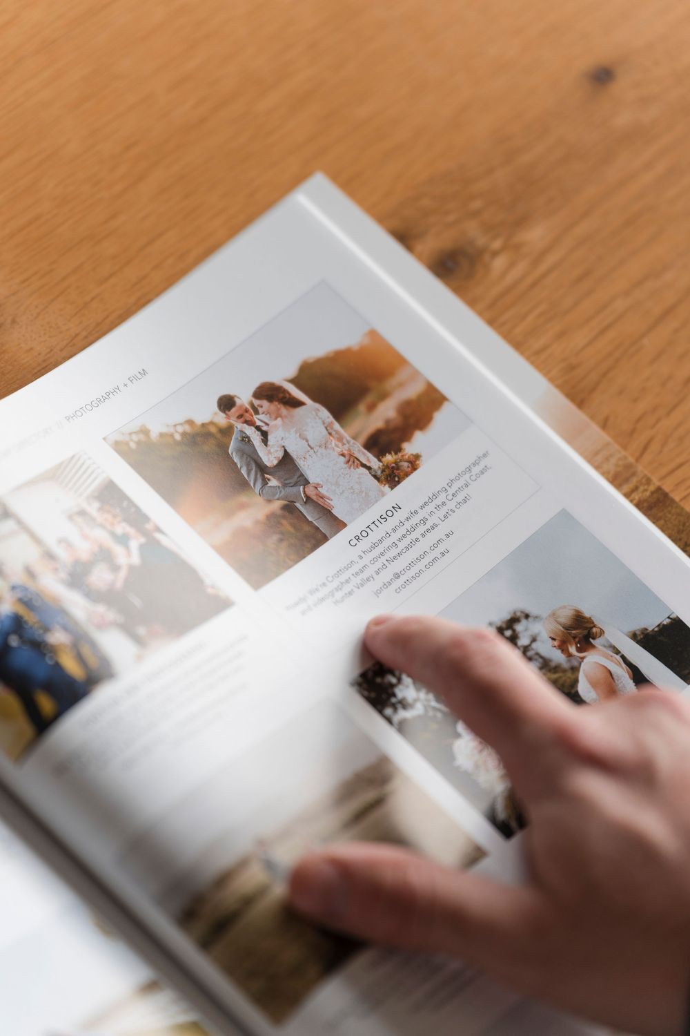 A hand flips through the pages of a photo album or book resting on a light wooden surface, creating a dynamic motion effect.