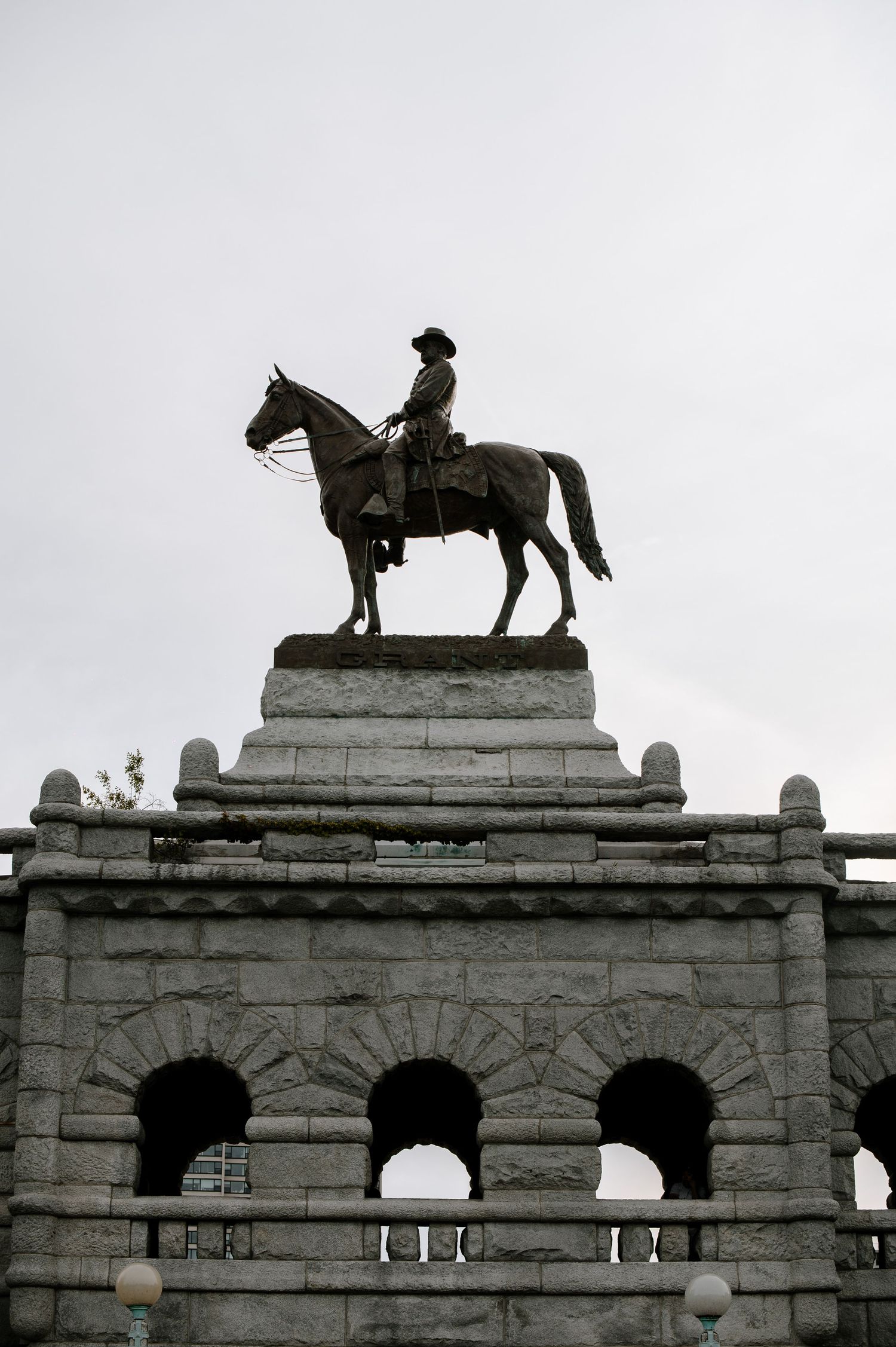 An equestrian statue silhouetted against a gray sky atop an arched stone structure with decorative elements.