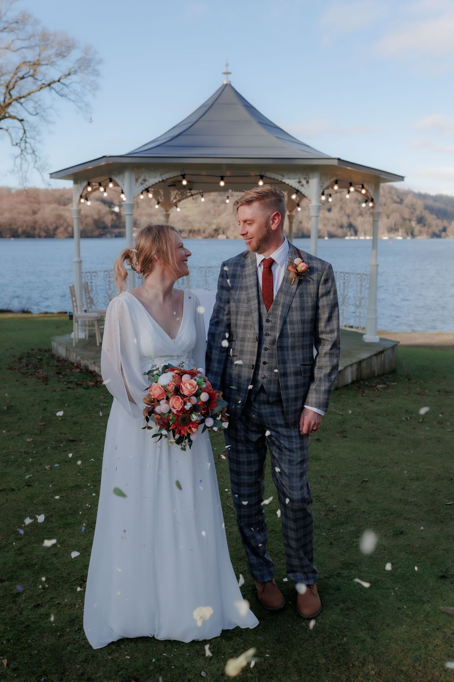 A wedding celebration featuring white flower petals falling in front of a lakeside gazebo.