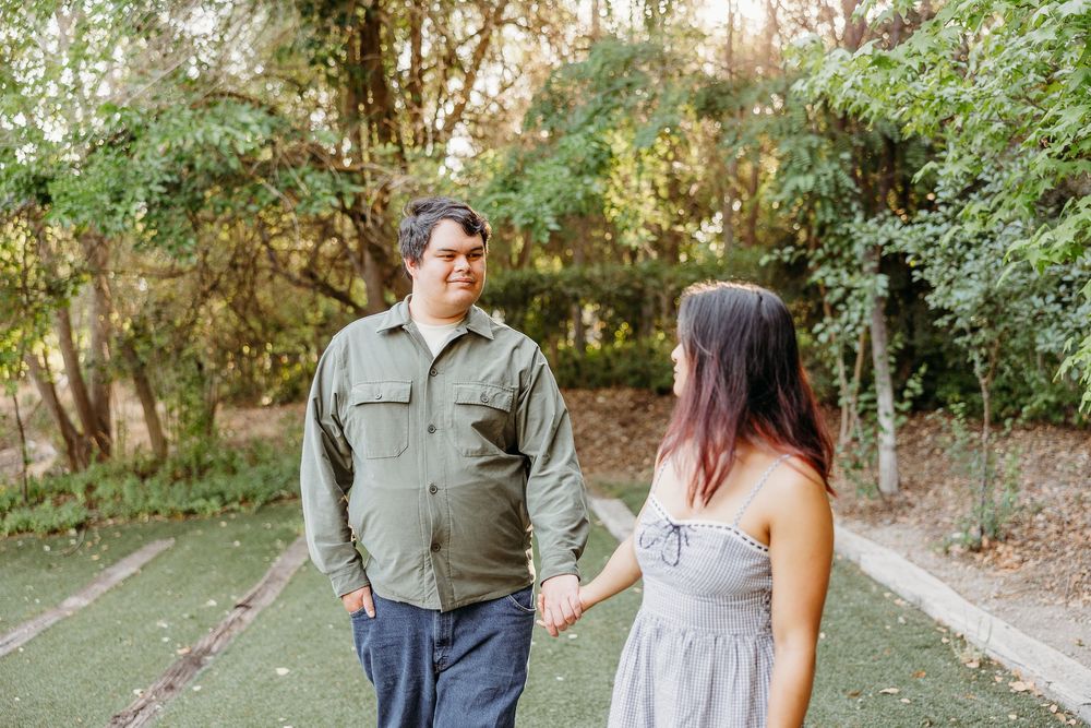 Engaged couple walks together through a lush wooded path during their outdoor engagement photo session.