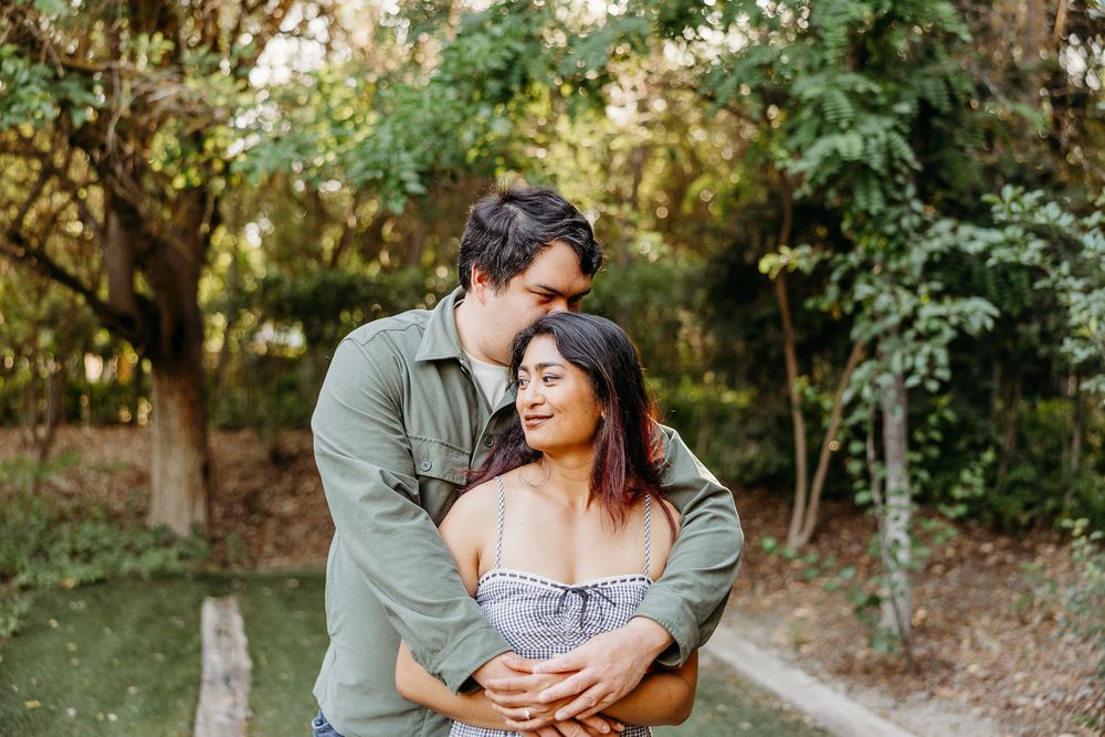 A romantic couple embraces outdoors in a garden setting during golden hour sunlight.