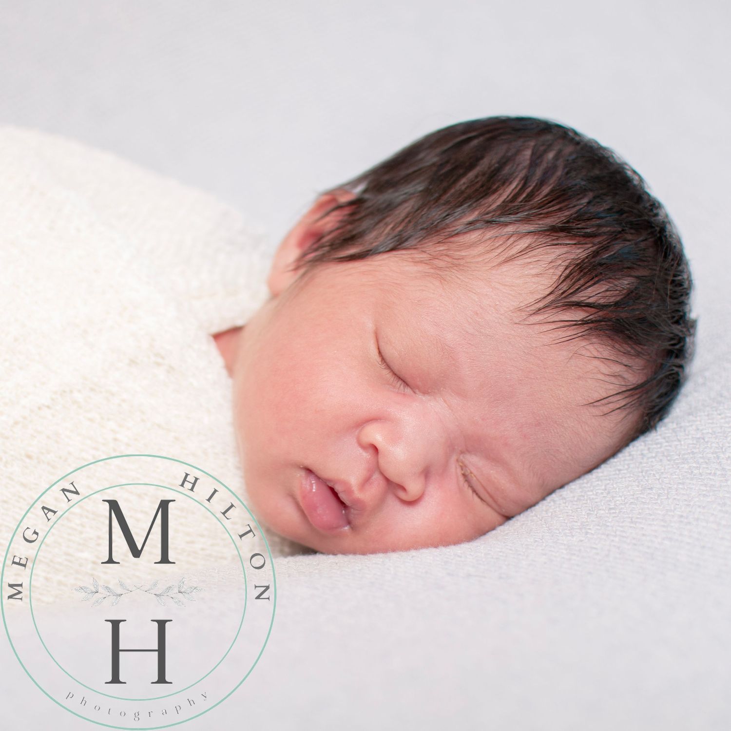 A sleeping newborn baby rests peacefully on white blankets in a professional portrait setting.