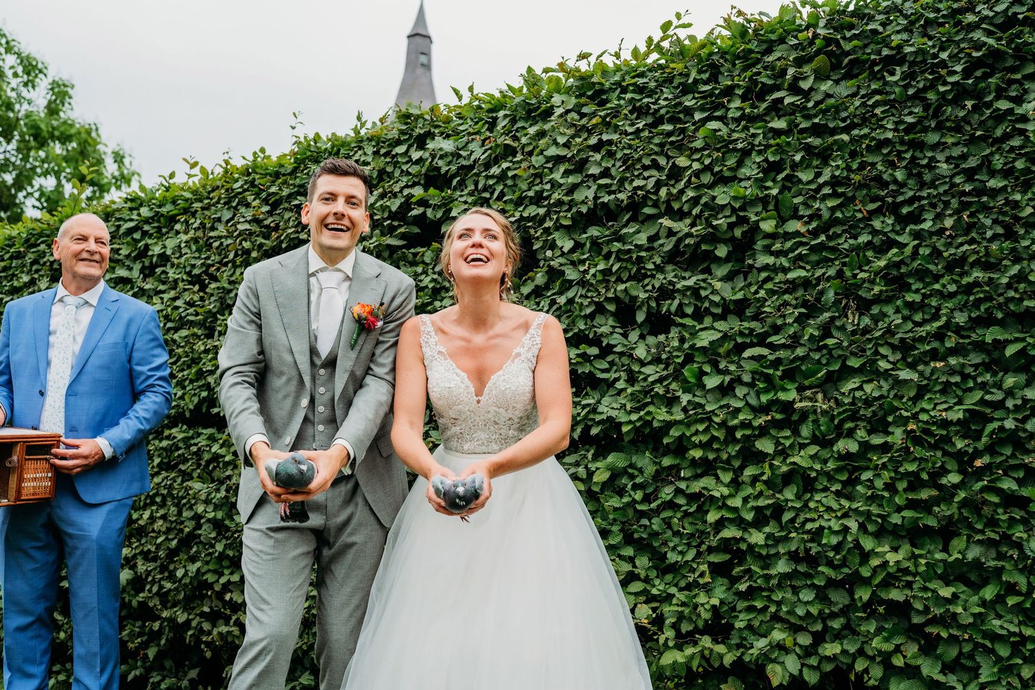 A wedding party stands together against a lush green hedge backdrop during an outdoor celebration.