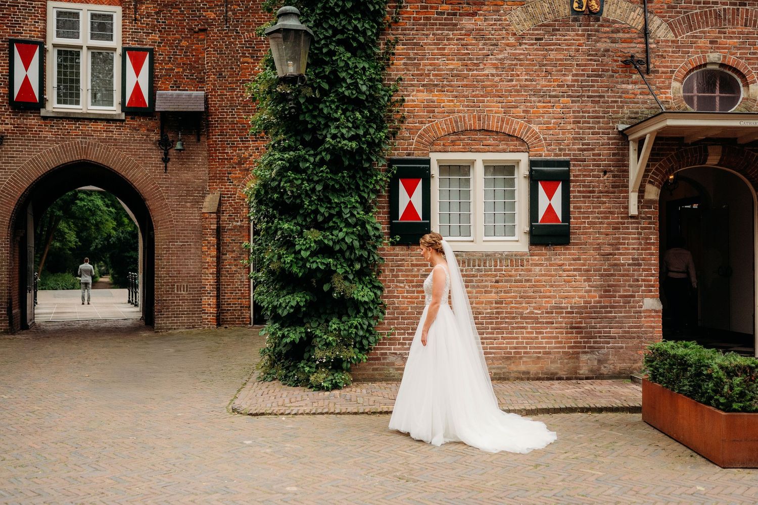 Historic brick building with ornate windows and archways features climbing ivy and elegant paved courtyard.