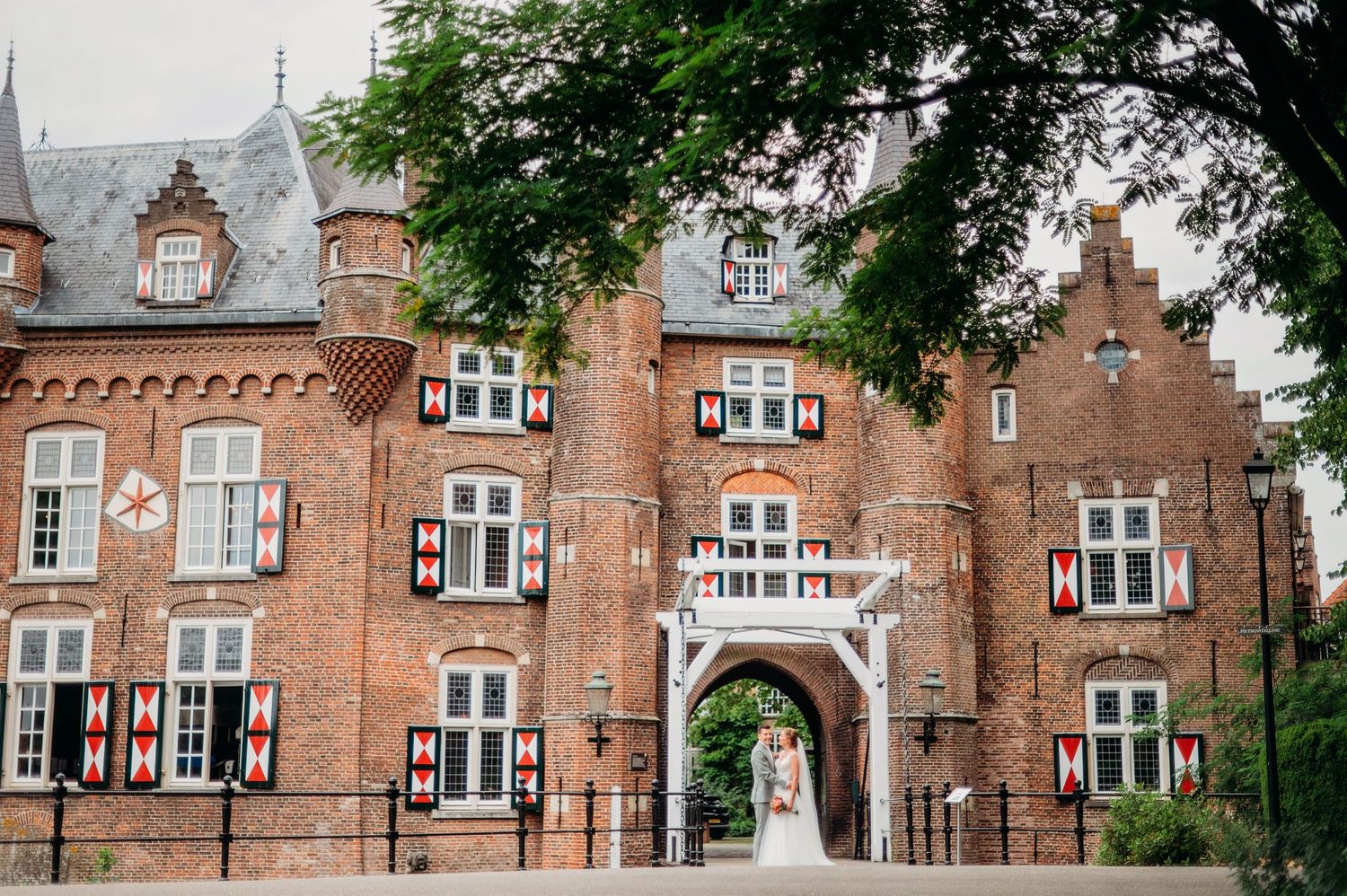 Historic red brick Tudor-style buildings with white-trimmed windows line a tree-shaded street in a quaint residential district.