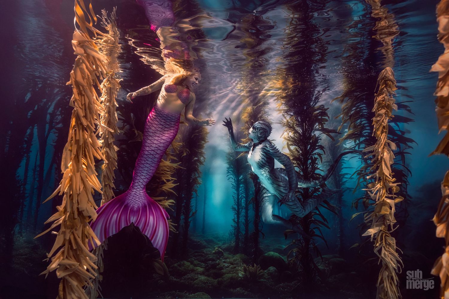 Two divers and a person in a purple mermaid tail pose underwater among kelp forests in mystical blue lighting.