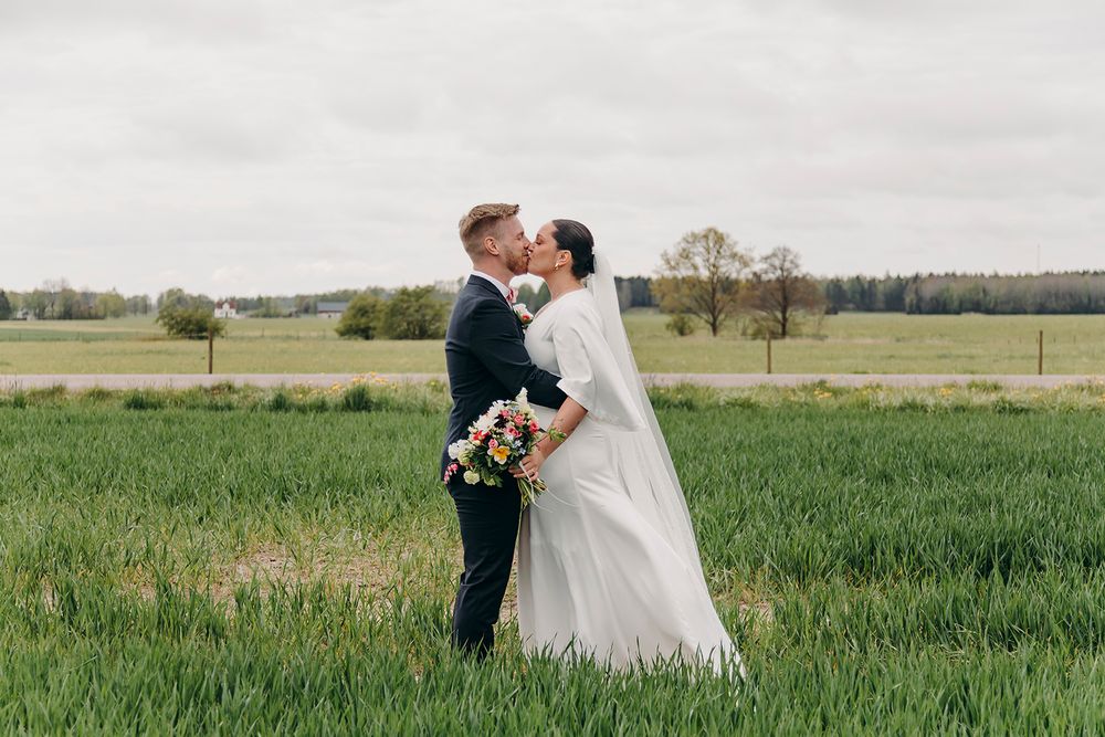 A couple shares a romantic moment in a lush green meadow during their wedding day, surrounded by open countryside.