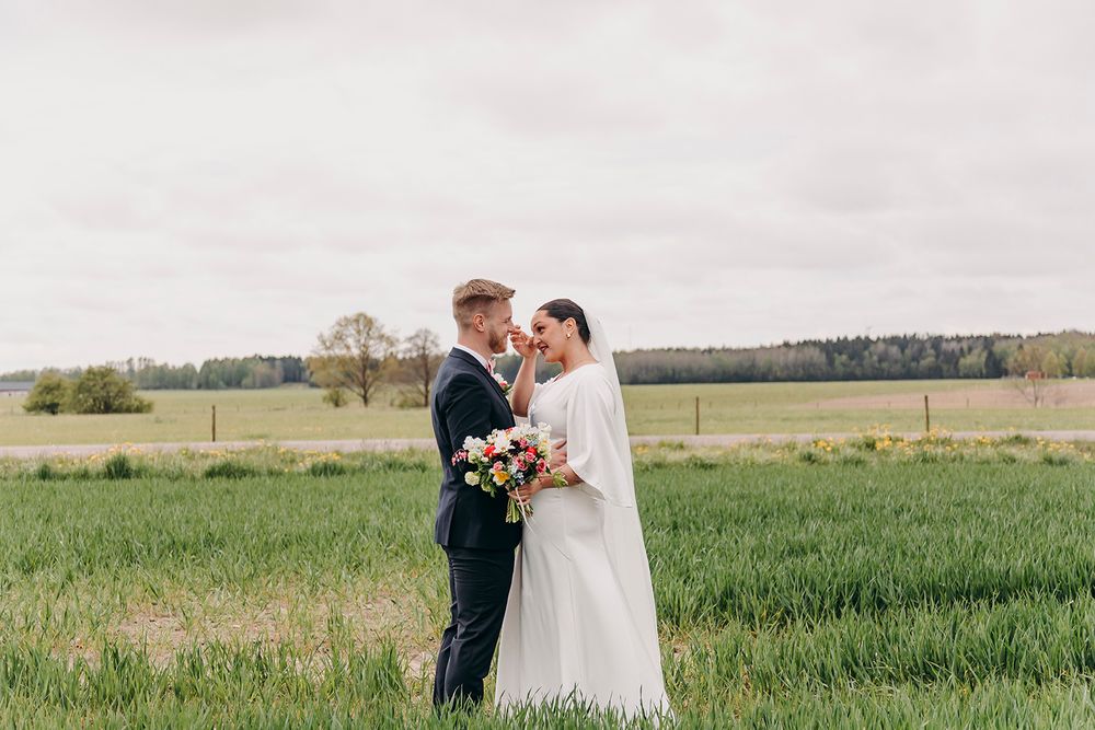 A bride and groom embrace in a beautiful green meadow on their wedding day with a rural landscape in the background.