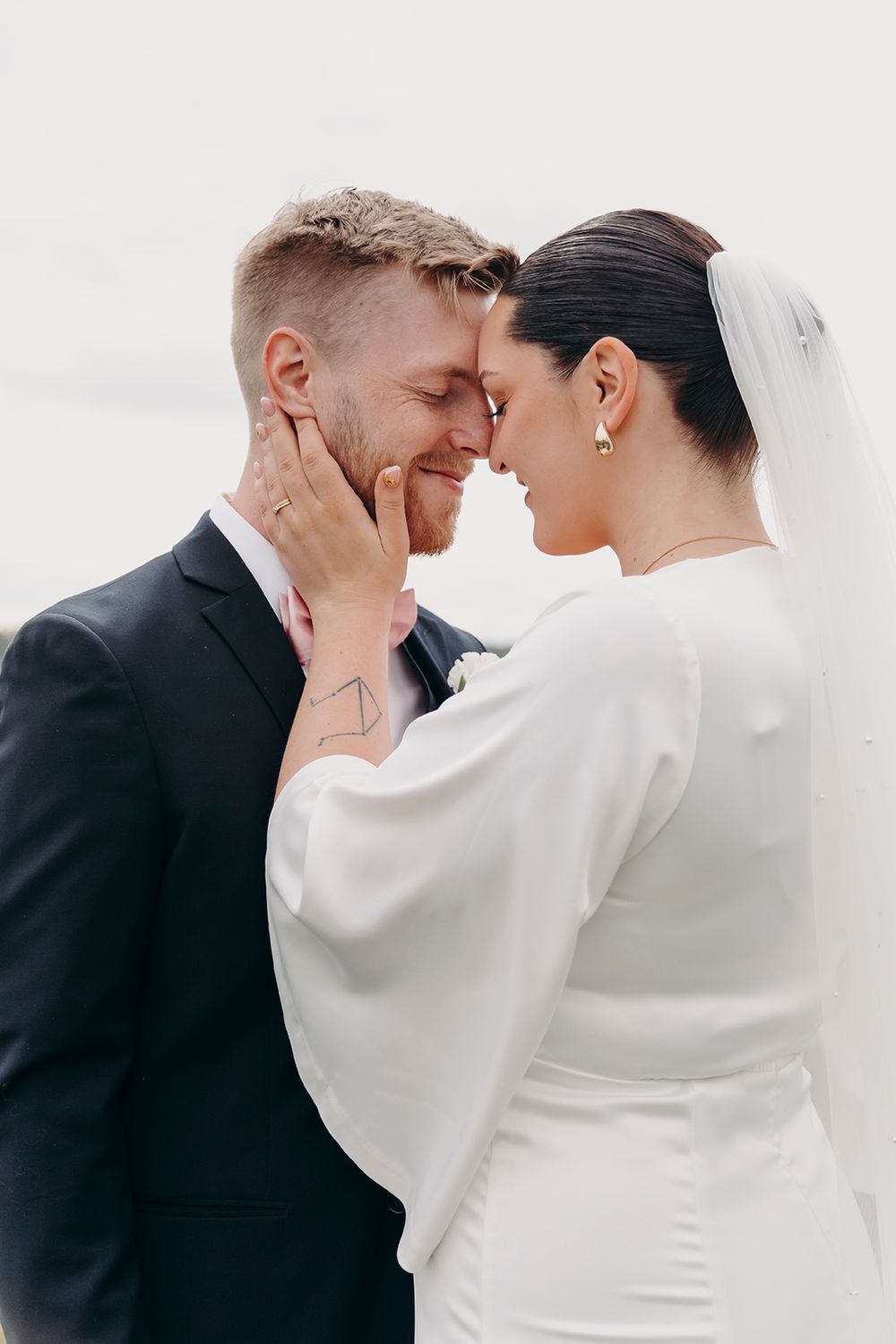 A loving couple in wedding attire share an intimate moment, with the bride in white and groom in black suit.