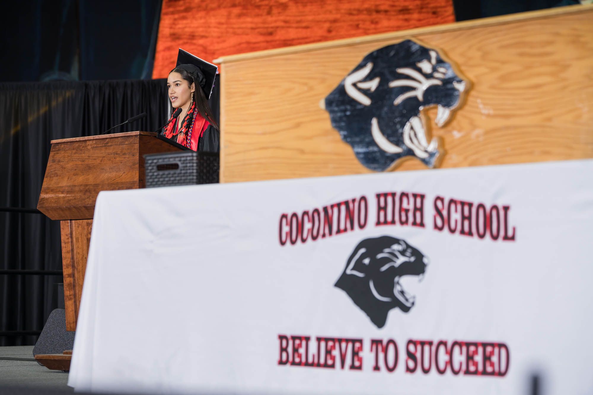 White banner displaying Coconino High School's panther mascot and motto 'Believe to Succeed' at podium. Yadira Ortiz Soto presents.