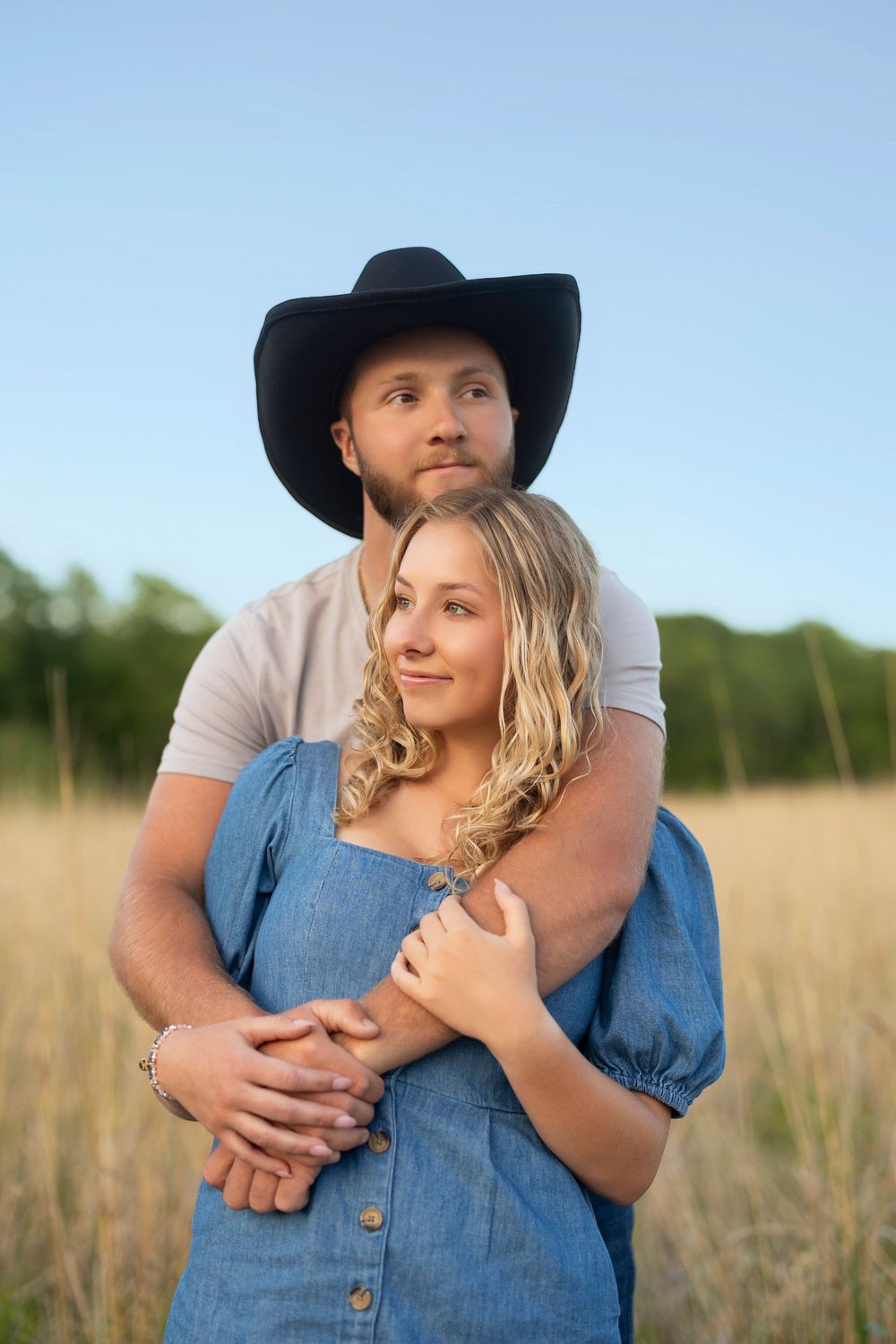 A tender moment captured in a wheat field as a couple holds each other close, with him wearing a western hat.