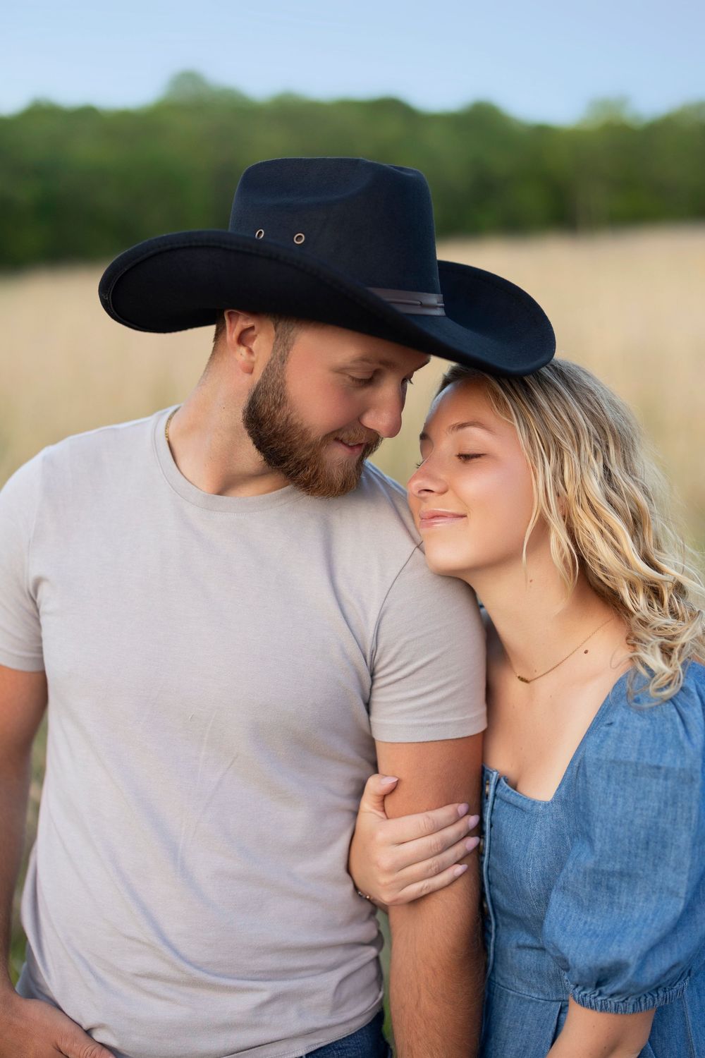A couple in a field wearing cowboy hats share an intimate moment at sunset.