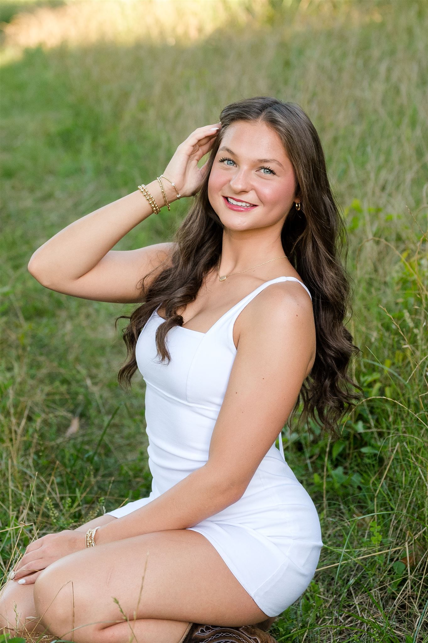 Outdoor portrait of someone in a white summer dress sitting in tall grass on a sunny day.