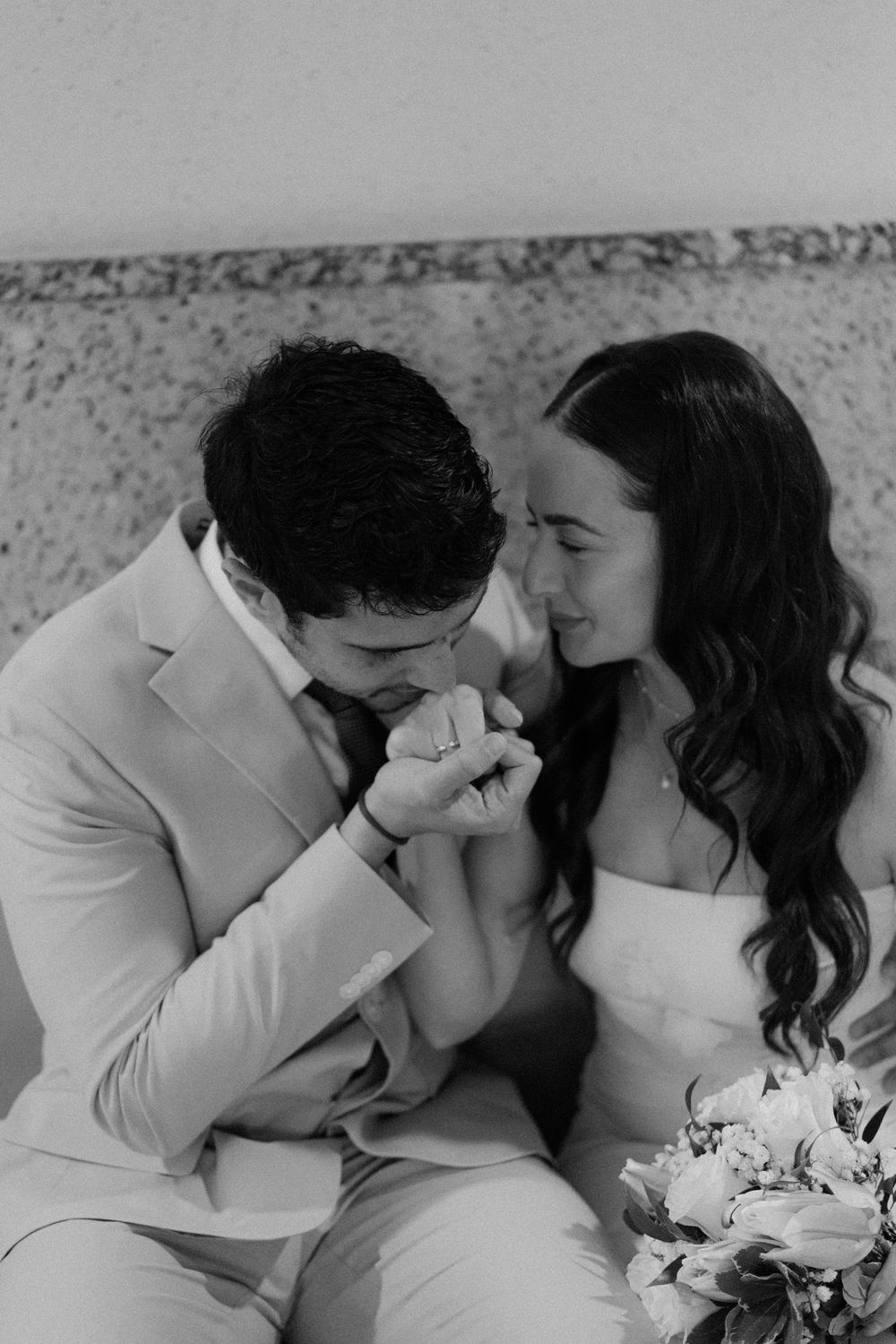 Black and white photo showing a tender moment between newlyweds as they share a close embrace with a bridal bouquet visible.