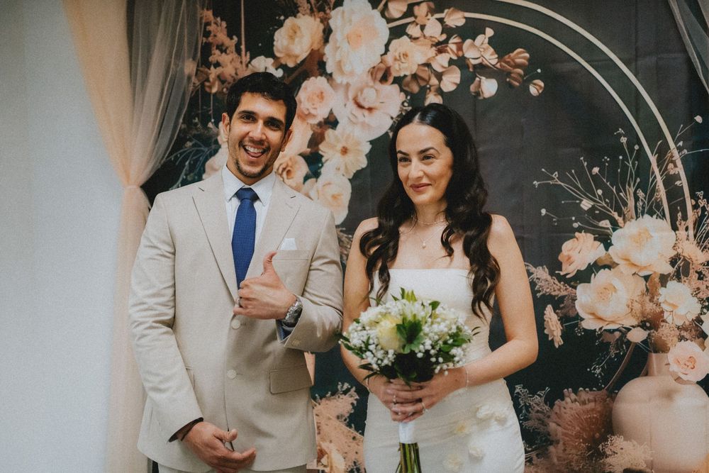 A couple celebrates their wedding day in front of a floral arch with peach roses and elegant decor.