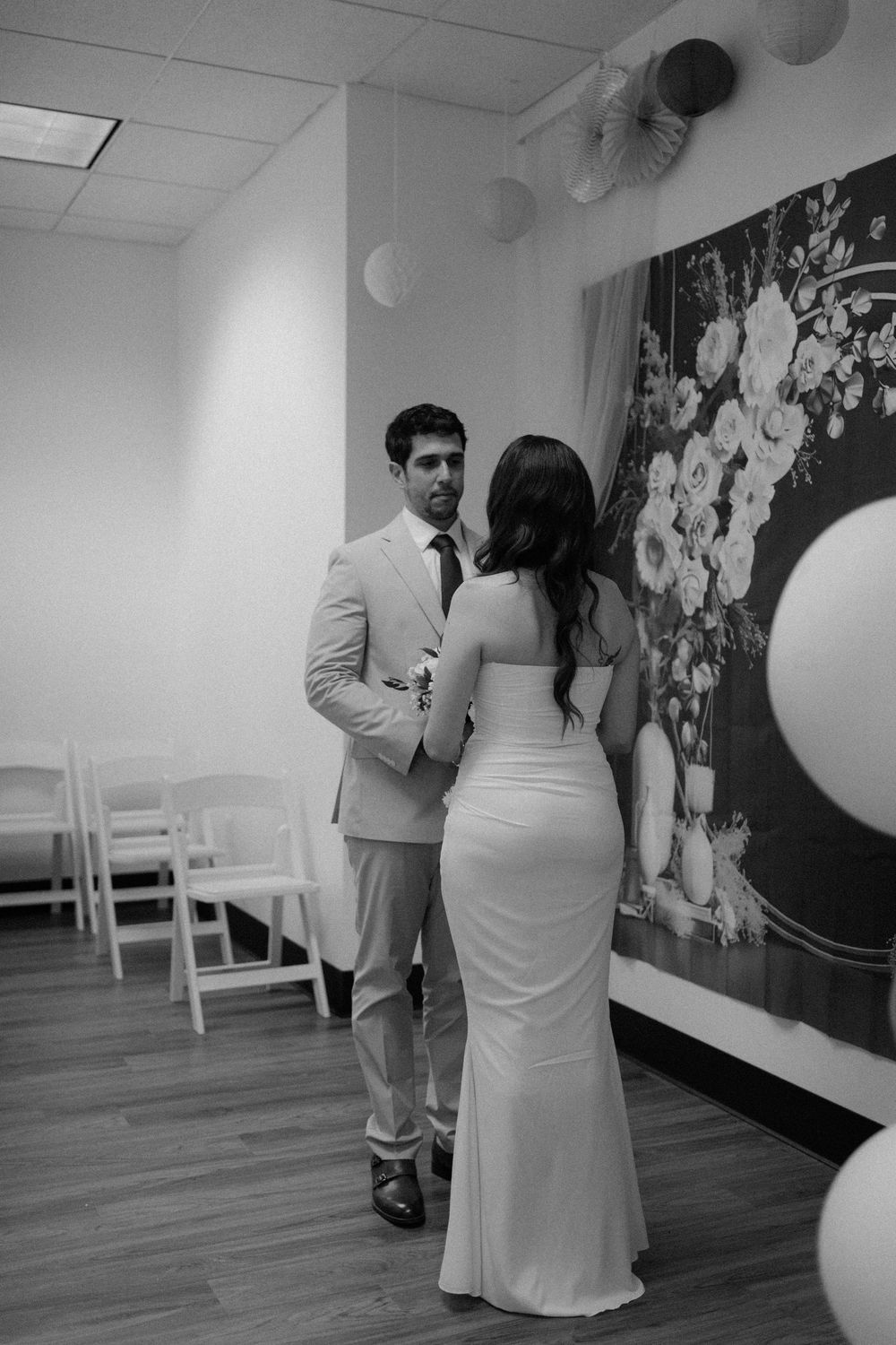 A couple shares an intimate moment in a room decorated with balloons and floral backdrop during their wedding ceremony.