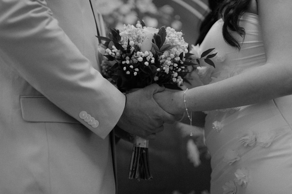 Black and white close-up shot of hands holding an elegant wedding bouquet with white flowers and baby's breath.