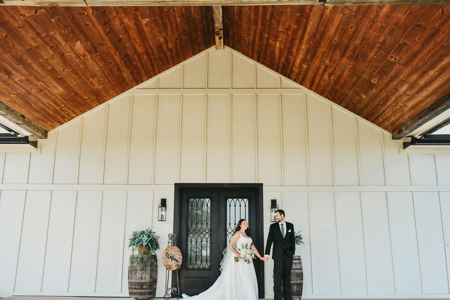 Full-length bridal portrait with groom and rustic Texas barn