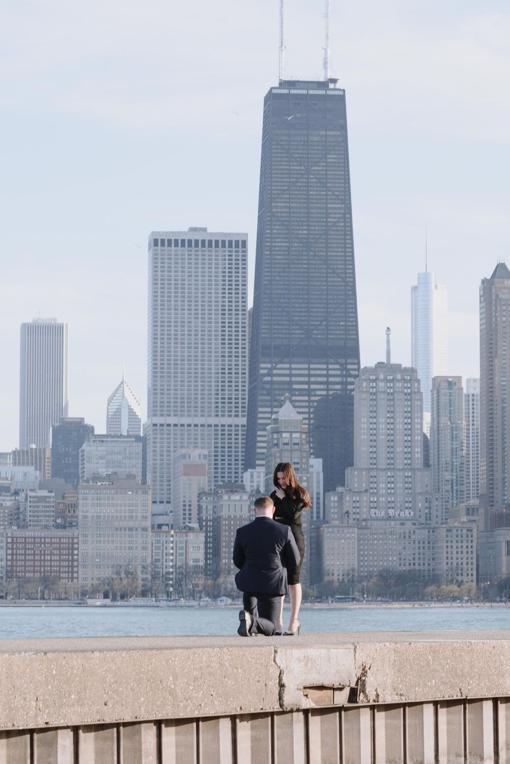 A couple sits on a ledge overlooking the Chicago skyline with the iconic John Hancock Center dominating the view.