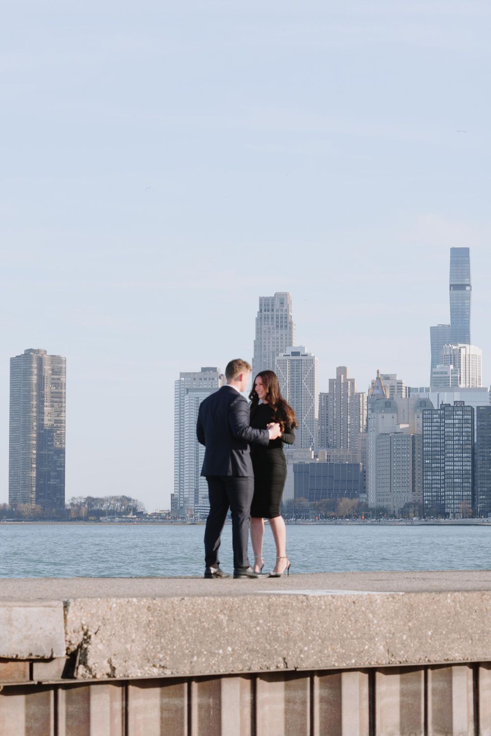 A couple stands intimately on a concrete pier overlooking Lake Michigan with Chicago's magnificent skyline in the background.